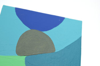 Peinture acrylique réalisée au couteau représentant un paysage onirique en format carré 10 centimètres par 10 centimètres sur carton entoilé. Un poème pictural où les formes et les couleurs remplacent les mots. Ce tableau se compose de couleur froides. Sur celui-ci on peut distinguer en arrière-plan un ciel représenté par un aplat bleu gris entourant deux rochers de forme arrondies en équilibre l’un sur l’autre, celui d’en dessous est gris foncé irisé et l’autre bleu. En bas à gauche un aplat vert qui s’emboite dans un aplat de bleu canard.